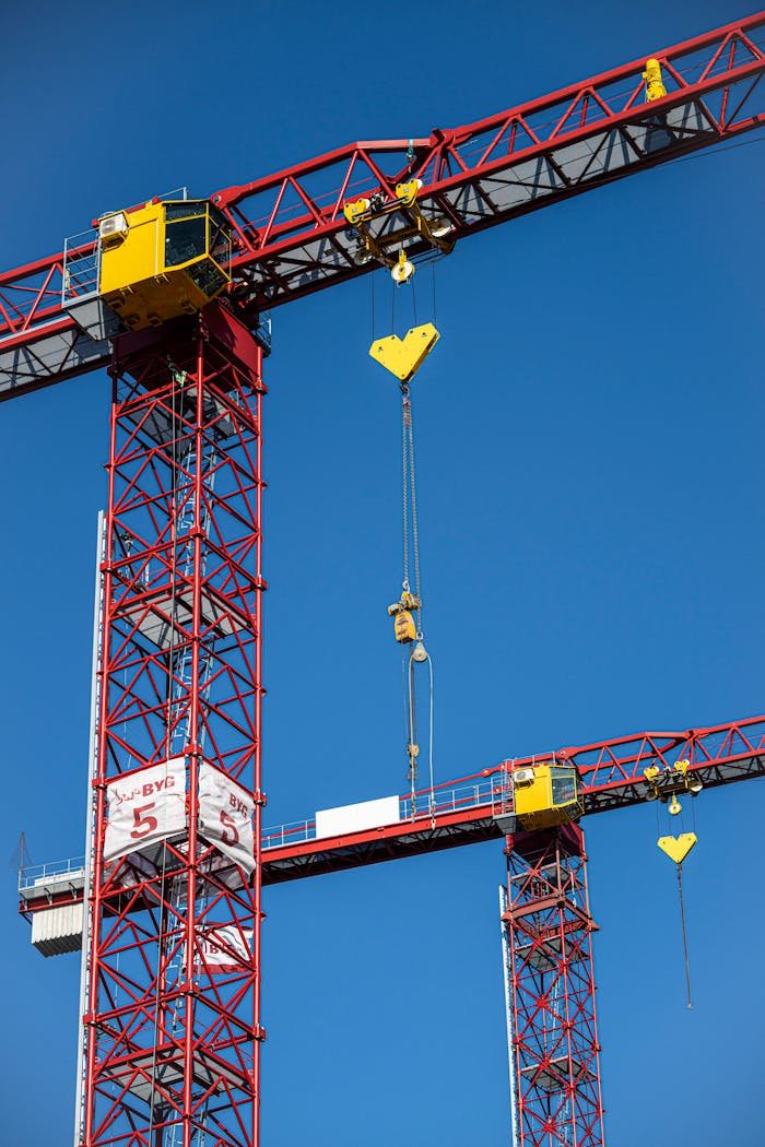 Red and yellow tower cranes against a blue sky, capturing modern construction machinery.